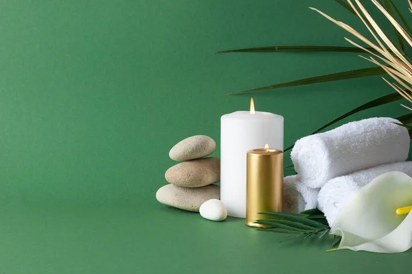 Spa treatment with herbal bag, candles and palm leaf on green background. Close up, copy space