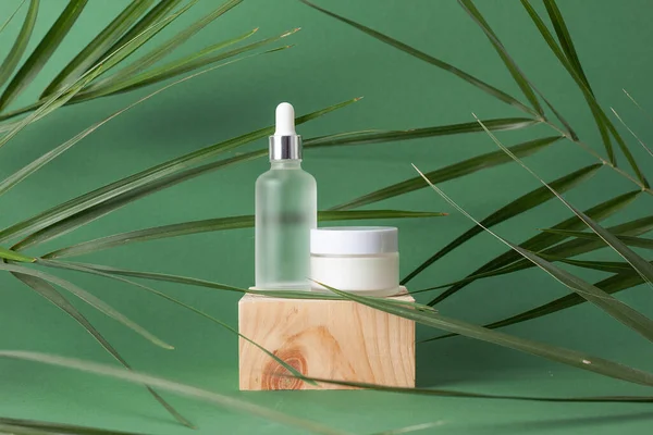 Cosmetic skin care products with wood podium and palm leaf on green background. Close up, copy space