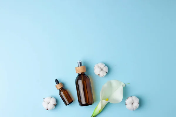 Cosmetic skin care products with flowers on blue background. Flat lay, copy space