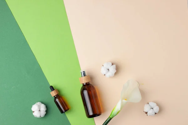 Cosmetic skin care products with flowers on green background. Flat lay, copy space
