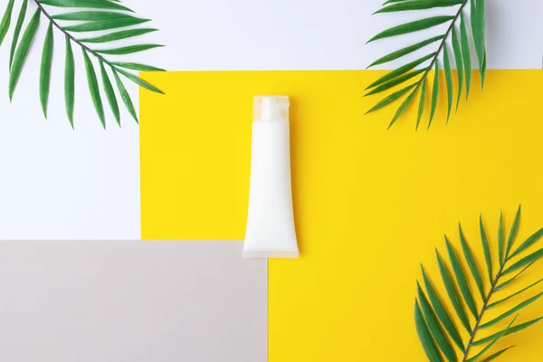 White tube of cosmetic cream with palm on yellow. Flat lay, copy space.