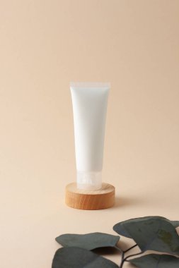 Beyaz kozmetik krem tüpü, okaliptüs ve bej arka planda tahta podyum. Kapat..