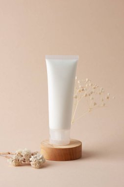 Beyaz kozmetik krem tüpü, bej arka planda tahta kürsüde çiçekler. Kapat..