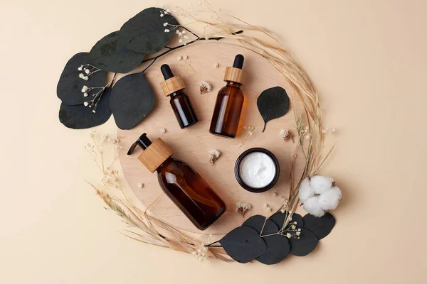 Cosmetic skin care products with flowers and wood on pastel beige background. Flat lay.