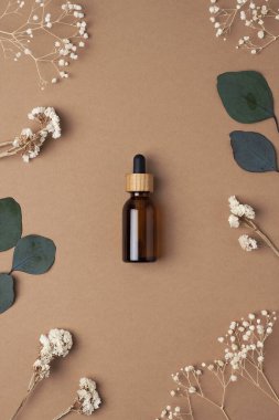 Çiçekli kozmetik şişesi ve kahverengi arka planda okaliptüs. Düz yatıyordu