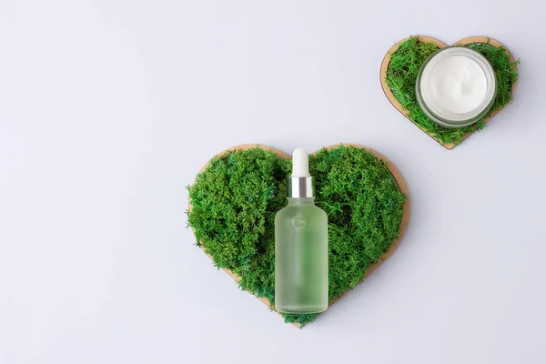 Cosmetic skin care products with a wooden heart and moss on white background. Flat lay, copy space
