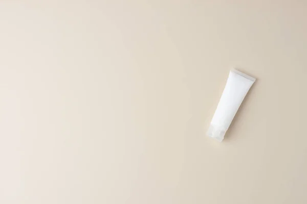 Cosmetic background with white tube of cosmetic cream on pastel beige. Flat lay, copy space