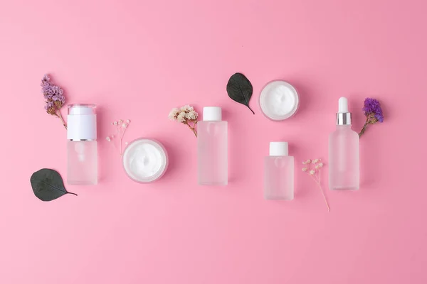 Skin care products on pink background with flowers, eucalyptus. Flat lay, composition.