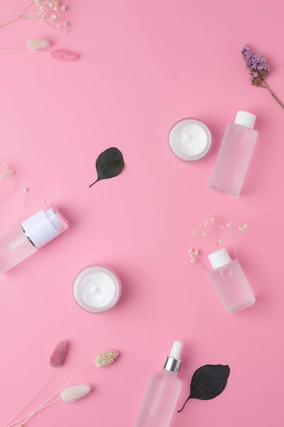 Skin care products on pink background with flowers, eucalyptus. Flat lay.