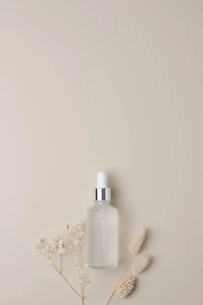 Cosmetic bottle with flowers on pastel beige background. Flat lay, copy space