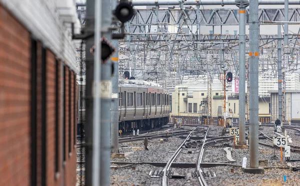 Train leaves leaves station past empty rails and mass of overhead wiring — Stock Photo, Image