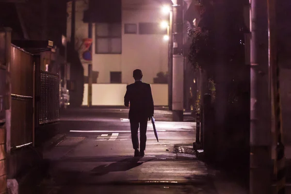 Yalnız iş adamı yağmurdan sonra gece eve yürür.