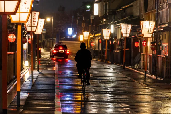 Samotny rowerzysta i taksówka na latarni drogi wyłożonej przez Kioto po deszczu — Zdjęcie stockowe