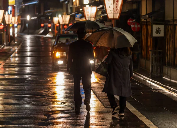 Para przewożących parasole spacery w kierunku taksówki w deszczową noc w zabytkowej dzielnicy Kioto — Zdjęcie stockowe