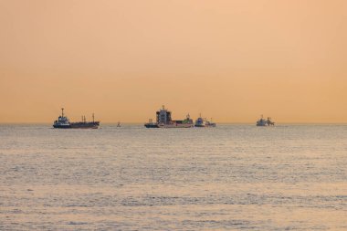 Gün batımında sisli ufukta üç farklı boyutta gemi.