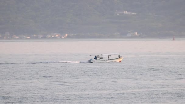 Small fishing boat slowly motoring along coast at golden hour — стоковое видео
