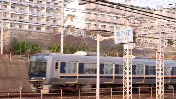 Пассажирский поезд движется по знаку города Кобе и жилым кварталам — стоковое видео
