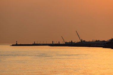Turuncu sis siluetli vinçler ve rıhtımdaki iskele üzerinde.