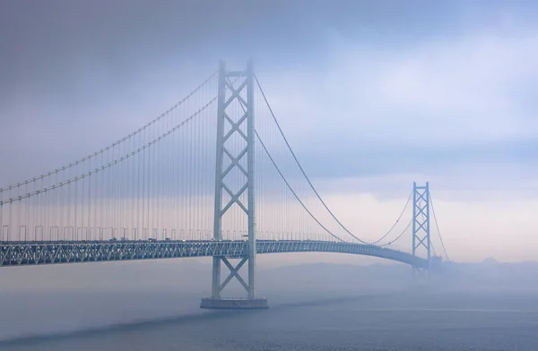 Ponte de suspensão em nuvens escuras e nevoeiro com toque de pôr do sol — Fotografia de Stock