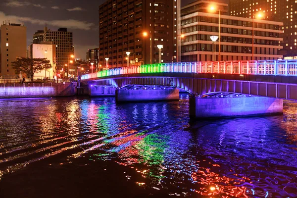 Gece şehir merkezinde nehir üzerinde renkli bir köprü.