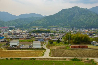 Arka planda dağlar olan küçük bir köyün yanındaki yolda T kavşağı boş.