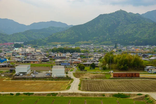 Arka planda dağlar olan küçük bir köyün yanındaki yolda T kavşağı boş.