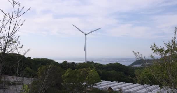 Wind turbine spinning over row of greenhouses under high clouds — Video