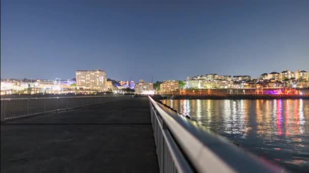 Trens zip por parque costeiro e edifícios à noite, panning timelapse — Vídeo de Stock