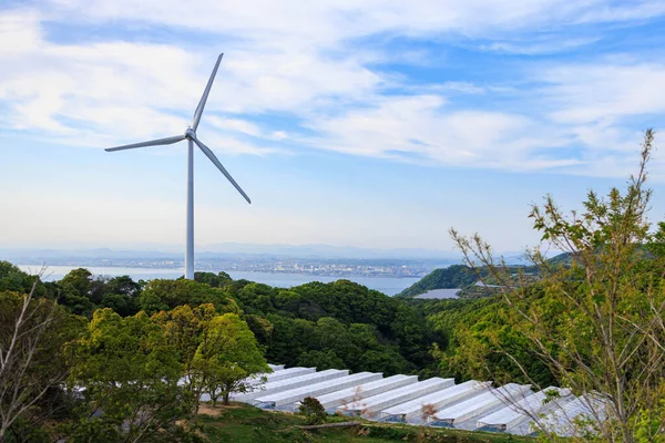 Wind turbine spinning over row of greenhouses under high clouds and blue sky — Stockfoto