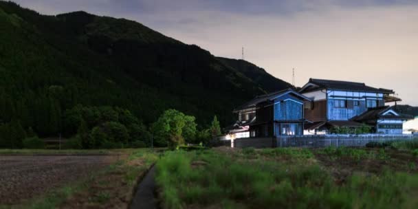 Timelapse of clouds moving over rural Japanese farm house lit by passing cars at night — Wideo stockowe