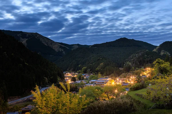 Karanlık dağlardaki küçük bir köyden gelen ışıklar gün batımından sonra bulutların altında