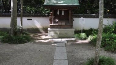 Narrow path leads to small shrine against white wall under trees