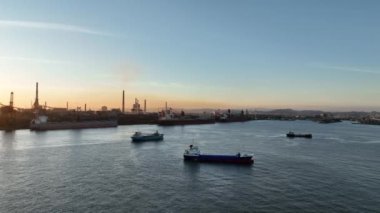 Küçük kargo gemisi gün batımında bacalardan endüstriyel limana yelken açar. Yüksek kalite 4k görüntü