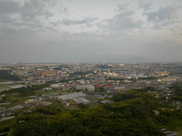 Alacakaranlıkta yeşil tepelerin kenarındaki genişleyen şehrin hava manzarası. Yüksek kalite fotoğraf