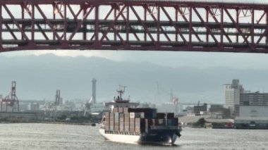 Osaka, Japan - July 10, 2022: Fully loaded cargo ship sails under bridge with light traffic. High quality 4k footage