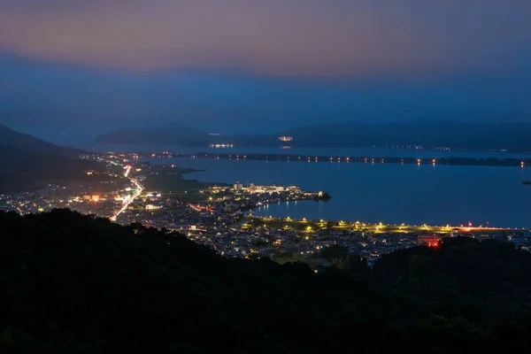 Akşamın erken saatlerinde Amanohashidate kara köprüsü ve şehir ışıkları manzarası. Yüksek kalite fotoğraf