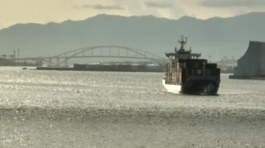 Late afternoon sun hits fully loaded cargo ship entering industrial harbor. High quality 4k footage
