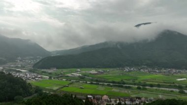 Aerial move over green rice fields and river towards misty mountain. High quality 4k footage