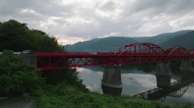 Red bridge over calm river towards mountains at dusk. High quality 4k footage