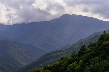 Distant mountain peak and forested valley visible through haze on cloudy day. High quality photo