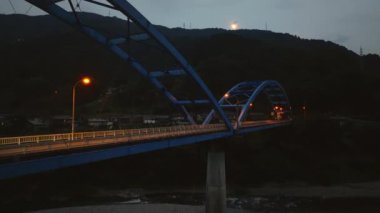 Single car moves over empty arched bridge toward dark mountain at night. High quality 4k footage