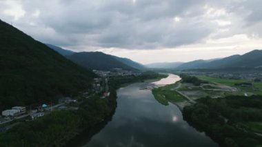 Descent over river at dusk reveals red bridge against mountain background. High quality 4k footage
