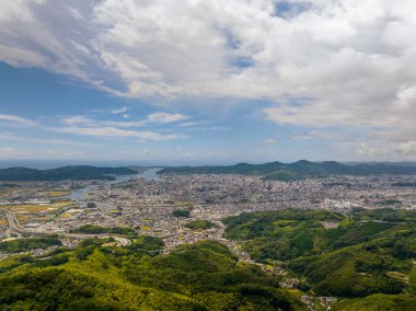 Aerial view of sprawling city at base of green hills. High quality photo