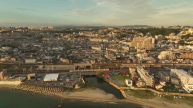 Train passes by apartments and sprawling coastal town on rolling hills. High quality 4k footage