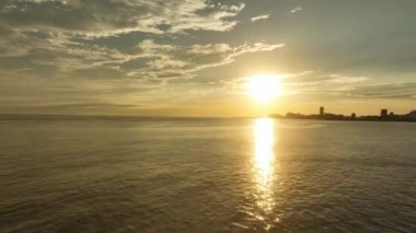 Flying low over small waves toward setting sun reflecting off calm water. High quality 4k footage