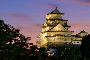 Himeji Castle, one of Japans famous historic sites, as crescent moon sets through beautiful sunset colors. High quality photo