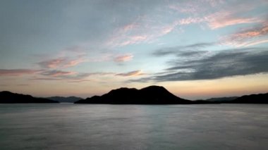 Flying low over calm seas with mountain island silhouetted against dawn sky. High quality 4k footage
