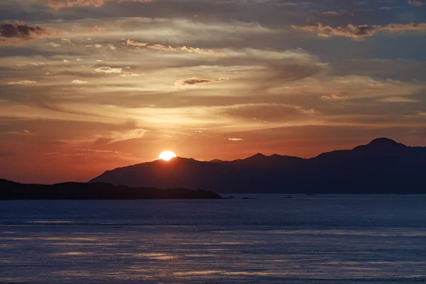 Güneş, kıyı adası açıklarındaki uzak mavi dağların ardında batar. Yüksek kalite fotoğraf