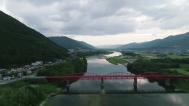 Güzel nehir boyunca kırmızı köprü ve alacakaranlıkta dağ manzarası. Yüksek kalite 4k görüntü