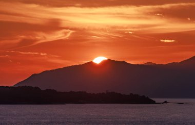Gökyüzü alacakaranlıkta turuncu parlarken güneş uzak dağların üzerinden yükselir. Yüksek kalite fotoğraf